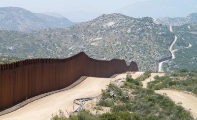 U.S./Mexico border with wall in foreground and mountains behind