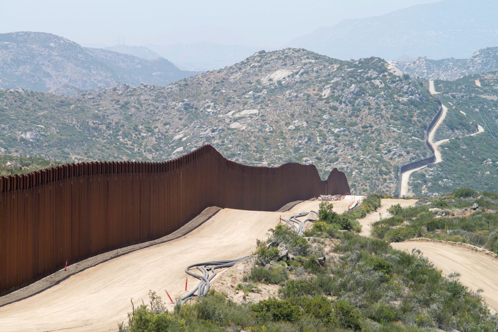 U.S./Mexico border with wall in foreground and mountains behind