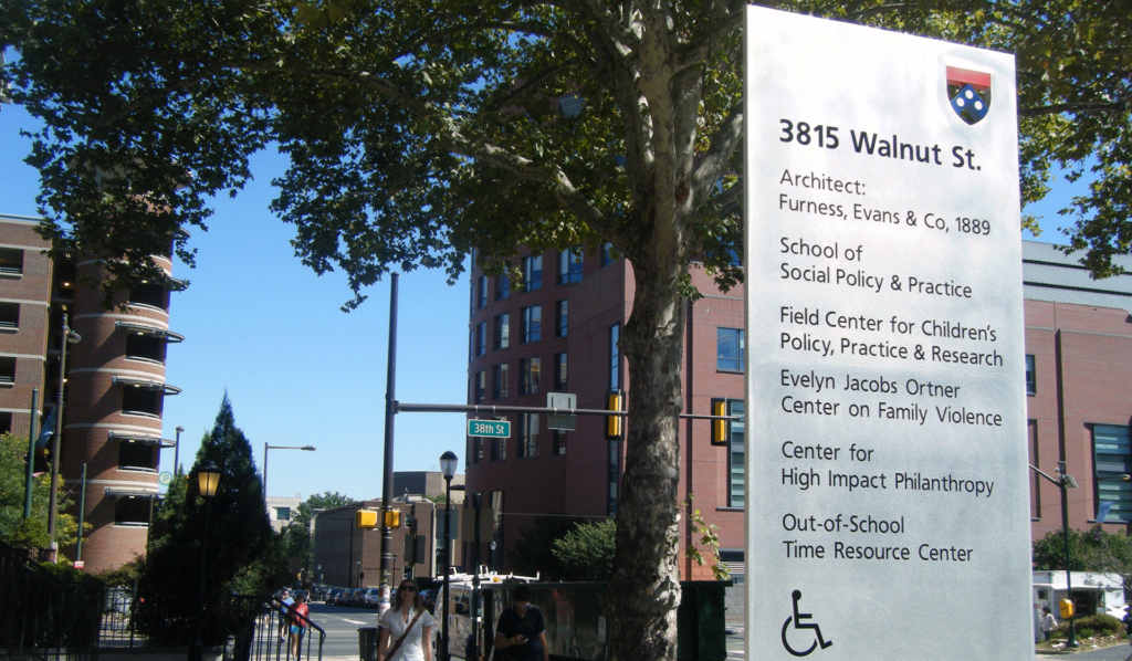 Signboard showing 3815 Walnut St and SP2's research entities, and buildings out of focus in background