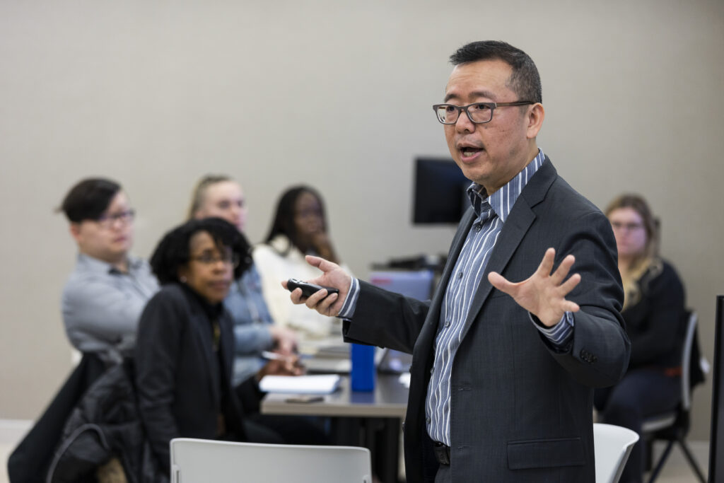 Dr. Chao Guo speaks to a class. Students can be seen listening in the background.