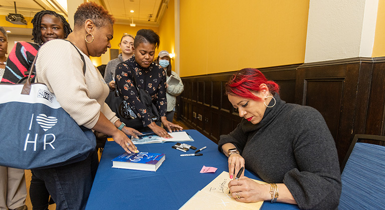 Nikole Hannah-Jones sits at a table signing copies of The 1619 Project before a long line of audience members.