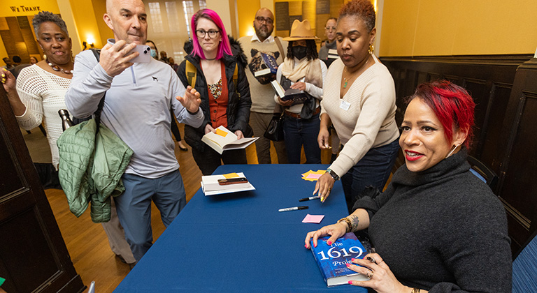 Audience members gather and take photos as Nikole Hannah-Jones prepares to sign a book at a table.