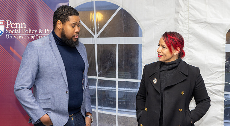 Nikole Hannah-Jones and an attendee interact at a reception in a white tent. A red and blue banner nearby shows the logo of Penn's School of Social Policy & Practice.