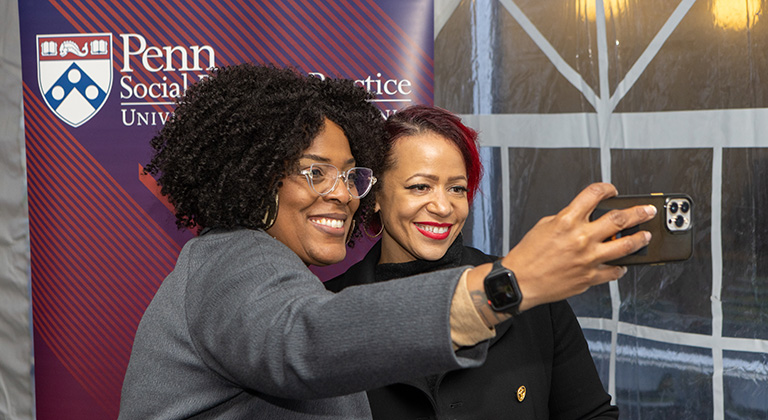 Nikole Hannah-Jones poses for an attendee's selfie. A red and blue banner behind them shows the logo of Penn's School of Social Policy & Practice.