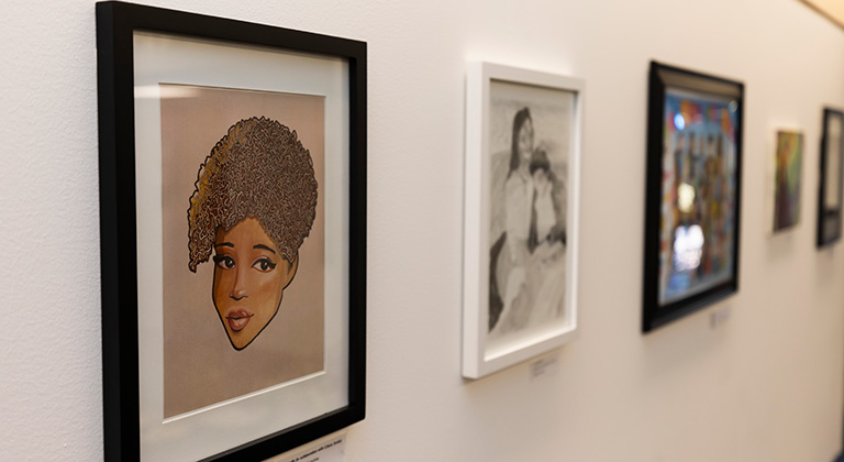 Five framed works of art appear in a row on the wall, shown at an angle. The nearest images are of a person's face and two people embracing.