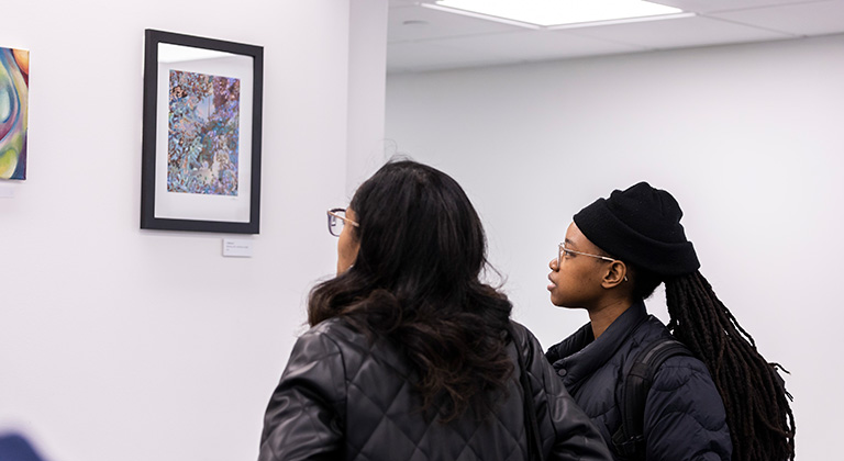 Two students look at a multicolored, framed work of art on the lobby wall.