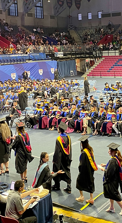 Graduating students walk in a line across the Palestra floor, before graduates sitting in rows and the audience in bleachers