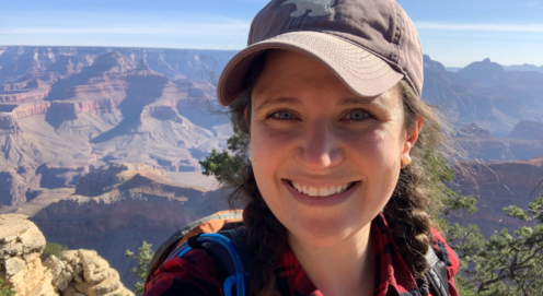 Headshot of Millan AbiNader at the Grand Canyon. Millan is wearing a hat, backpack, and red plaid shirt.